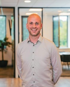 Man in light shirt in office smiling at the camera